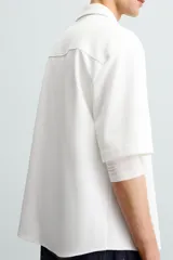 Sobrecamisa negra de tejido con elasticidad, cuello solapa y manga corta. Tiene dos bolsillos de plastrón en el pecho y cierre frontal con botones a presión.