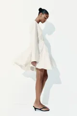 Vestido corto blanco con escote en V profundo, mangas largas con abertura en los puños, cierre oculto en la espalda y cinturón fino extraíble.