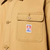 Campera de trabajo Wrangler color beige, de corte recto, con cuello clásico, cierre frontal con botones a presión, tres bolsillos frontales con solapa y botón, puños ajustables con botón y etiqueta tejida con el logo de la marca en el bolsillo superior.