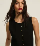 Chaleco negro de sastrería con cuello redondo, cierre frontal con botones metálicos y lazo cruzado en la espalda.