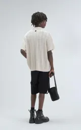 Camisa de tejido de punto color beige, manga corta, con cuello polo y cierre frontal de botones. Presenta un calce regular y un patrón calado en zigzag.