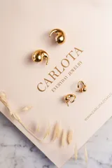 Par de aros dorados con forma de coma, de acero quirúrgico con baño de oro.