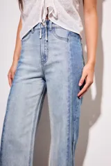 Jean de tiro medio, corte recto y largo cropped, confeccionado en denim de algodón con elastano. Presenta un efecto de lavado bicolor o combinado, con paneles de diferente tono de azul claro, y costuras verticales marcadas en el frente. El ruedo es deshilachado.