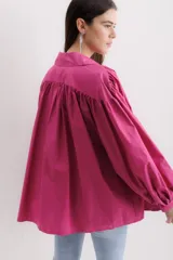 Camisa fucsia de algodón, corte holgado, con cuello camisero, cierre frontal con botones y mangas largas abullonadas con puños abotonados.