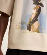 Remera overboxy color crema con estampa frontal de una mujer con un pájaro en la cabeza y lettering bordado.
