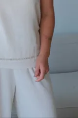 Musculosa color crudo, de corte recto y sin mangas, con cuello redondo. Presenta un detalle de pespunte horizontal a la altura de la cadera.