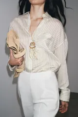 Camisa de manga larga con cuello solapa, a rayas verticales grises y blancas. Tiene un bolsillo de plastrón en el delantero y cierre frontal con botones.