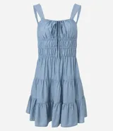 Vestido corto color beige, con escote recto, breteles medianos y lazo decorativo en el centro del busto. Presenta costura fruncida en la cintura y falda con babados en capas.