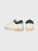 Championes Golden Goose modelo Super Star, de cuero blanco con estrella calada en el lateral, talón en cuero negro y suela color crema con efecto desgastado.