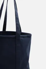 Bolso tipo shopper color azul marino, fabricado en tejido de algodón. Tiene doble asa de mano y un bolsillo plano en el interior.