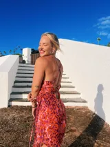 Vestido midi con estampado tie-dye en tonos rosados, azules y beige. Tiene escote drapeado, breteles finos y falda irregular con abertura lateral.