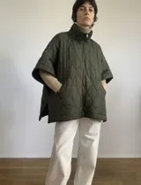 Poncho acolchado color mostaza con cuello alto y abertura frontal con cierre. Presenta un patrón capitoné de formas ovaladas y bolsillos delanteros.