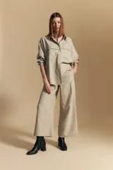 Camisa de manga larga color blanco hueso con finas rayas verticales en color oscuro. Presenta cuello camisero, botones frontales y dos bolsillos superpuestos en el pecho.