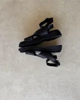 Sandalias bajas color gris topo, con tiras anchas cruzadas sobre el empeine y tobillera con hebilla metálica. Suela plana de goma negra.