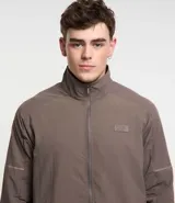 Campera deportiva color marrón, con cuello alto, cierre frontal con cremallera, manga larga, bolsillos laterales y detalles de etiqueta aplicada y rayas.