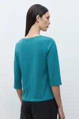 Remera verde petróleo con escote en V, mangas tres cuartos y diseño de broderie calado.