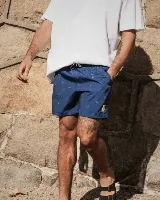 Short de baño azul con estampado de tablas de surf blancas, cintura elástica con cordón ajustable y bolsillos laterales.