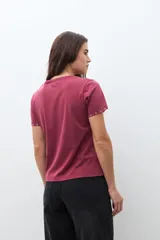 Remera de manga corta color bordó con cuello redondo y pequeños ojalillos metálicos decorativos en los bordes de las mangas.