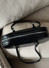Cartera tipo baguette de cuero sintético color negro con doble asa corta y cierre superior con cremallera.