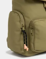 Mochila color beige con detalles en negro. Tiene solapa con tira de ajuste y broche, correas regulables, manija superior, bolsillo frontal con cierre y puller de cordón y goma, bolsillos laterales con cierres y pullers de cordón y goma, y tag de goma.