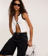 Musculosa blanca sin mangas, con cuello redondo y cierre frontal con cremallera. Presenta detalles contrastantes en negro en cuello y sisas. Diseño seamless.