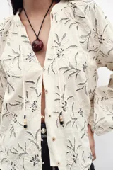 Blusa color crema con bordado floral en azul, de cuello redondo con cordón ajustable y mangas largas abullonadas con puños elásticos.