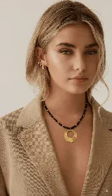 Collar corto con cuentas facetadas negras y medalla circular dorada.