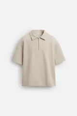 Polo color beige de corte relaxed fit, confeccionado en tejido interlock de algodón con elasticidad. Tiene cuello solapa y cierre frontal de cremallera.