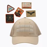 Gorro de estilo trucker color beige con paneles frontales de gabardina y paneles traseros de malla. Cuenta con visera curva, ajuste snap trasero y dos tiras de velcro horizontales en el frente para colocar parches. Incluye cinco parches de la marca Merrell con diferentes diseños.