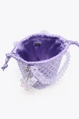 Bolso mini saca cilíndrica con cuerpo de cuentas transparentes y bolsita interior de tela satinada color lila con cierre fruncido. Incluye charm extraíble con forma de cubo.
