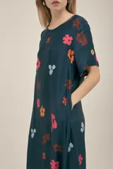 Vestido largo azul marino con estampado de flores en tonos naranja, rosa y celeste. Tiene corte holgado, mangas cortas y bolsillos laterales.