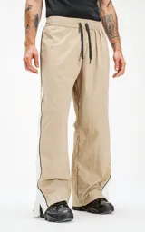 Pantalón deportivo beige de nylon con cintura elástica ajustable con cordón, corte holgado y aberturas laterales con broches.
