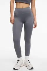 Calza deportiva larga color gris, con cintura alta, detalles de transparencias laterales en tul y bolsillos laterales.