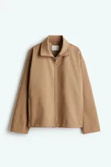 Campera color beige de sarga con cuello, cierre oculto adelante y bolsillos laterales con cierre. Modelo de corte holgado con pinzas en los codos para dar forma y cordón para ajustar elástico con topes en el bajo. Sin forrar.