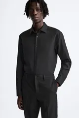 Camisa blanca de corte regular, cuello italiano, manga larga con puños abotonados y cierre frontal con botones.
