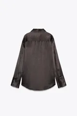 Camisa negra de satén con cuello solapa, manga larga, bolsillos con solapa en el delantero, bajo asimétrico y cierre frontal con botones.