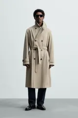 Trench largo regular fit color beige confeccionado en tejido italiano repelente al agua. Tiene cuello con solapas de pico, manga larga con puño ajustable con trabilla, bolsillos de vivo en cadera, bolsillo interior, cinturón del mismo tejido en cintura, bajo con abertura en centro espalda y cierre frontal de botonadura cruzada.