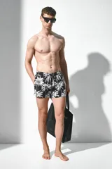 Short de baño negro con estampado de palmeras blancas, cintura elástica con cordón ajustable, bolsillos laterales y trasero.