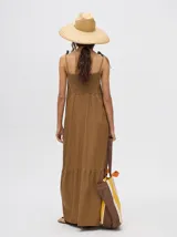 Vestido midi de denim algodón color marrón, con escote recto y tirantes finos ajustables con lazos. El corte es suelto y termina con un ruedo con semi-volado.