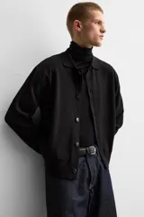 Camisa de punto color negro, corte relaxed fit, con cuello solapa, manga larga y cierre frontal con botones.