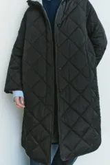 Chaqueta larga acolchada color negro con capucha y manga larga. Tiene bolsillos delanteros y bajo asimétrico con aberturas laterales. El cierre frontal es con botones ocultos por solapa.