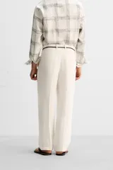 Pantalón color crema de lino, corte amplio, con pliegues frontales, bolsillos laterales y traseros de ojal. Cierre frontal con cremallera y gancho metálico oculto.