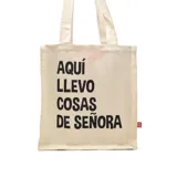 Bolso tipo tote bag de tela color crudo con asas cortas y estampado negro con la frase "Aquí llevo cosas de señora".