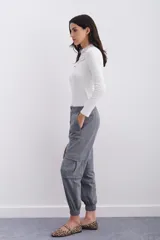 Pantalón de corderoy gris, de corte holgado, con elástico en la cintura, cierre y botón. Tiene bolsillos aplicados en el delantero y puños con elástico interno.
