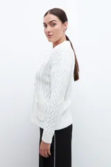 Cardigan crudo de tejido de punto trenzado, con cuello polo, cierre frontal con botones y bolsillos delanteros.