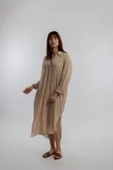 Vestido camisero midi color beige, de corte holgado, con cuello camisero, mangas largas con puños abotonados y aberturas laterales en el ruedo.