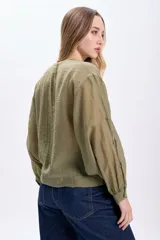 Camisa casual manga larga color verde oliva, de tela traslúcida con textura sutil. Tiene cuello redondo, cierre frontal con botones y mangas largas con puños elásticos.