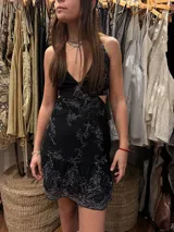 Vestido corto de lentejuelas color verde oliva, con escote en V, breteles finos cruzados en la espalda, cut-outs laterales y volado en el ruedo.