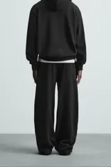 Pantalón jogger wide fit negro confeccionado en tejido de algodón con interior rizo. Pernera ancha, cintura elástica ajustable con cordón interior, bolsillos laterales y bolsillo trasero de plastrón.