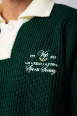 Sweater de punto verde con cuello polo color crema y bordado frontal con texto en blanco.